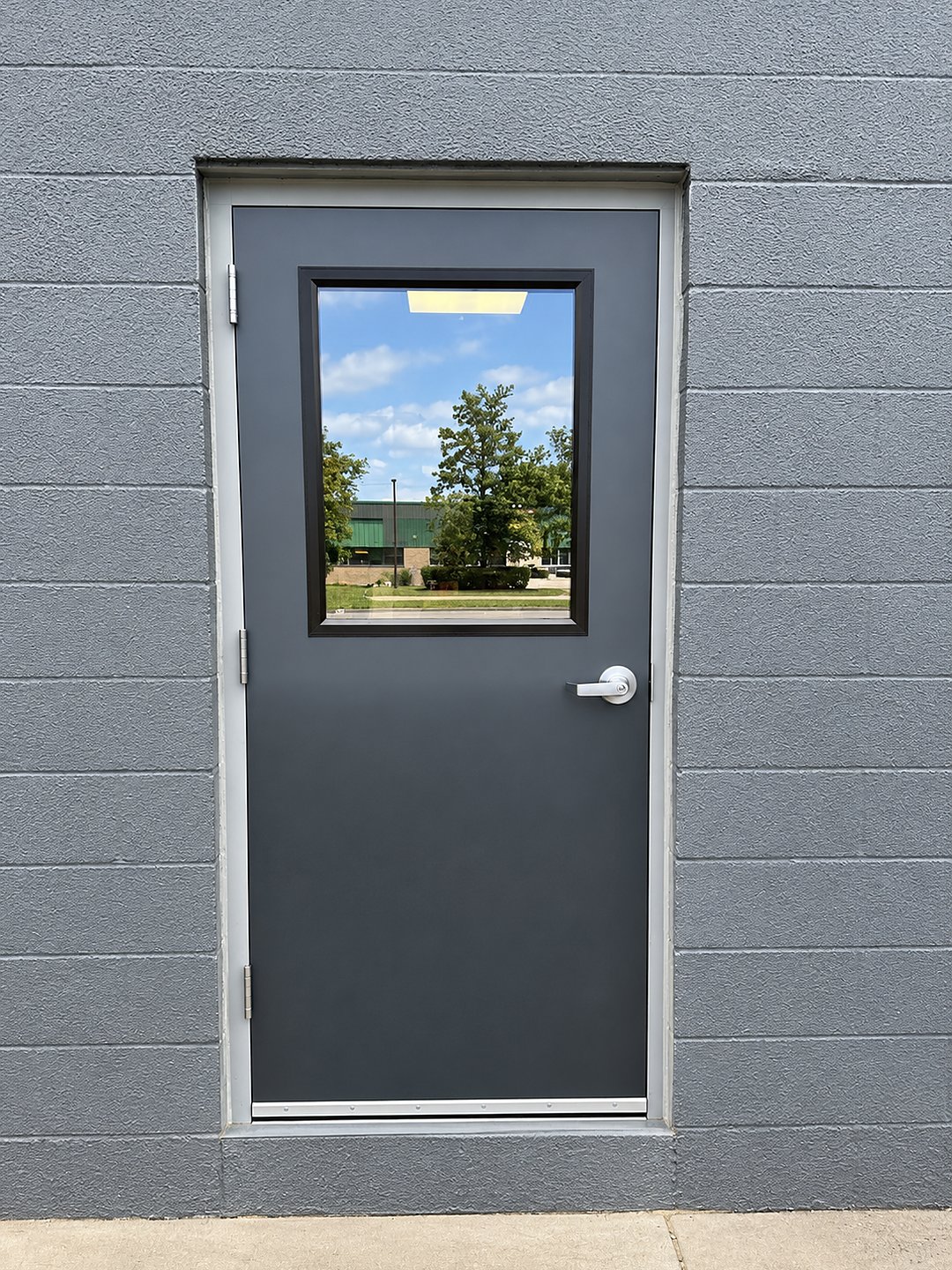 After: a new charcoal steel door and frame with a glass vision window and lever handle