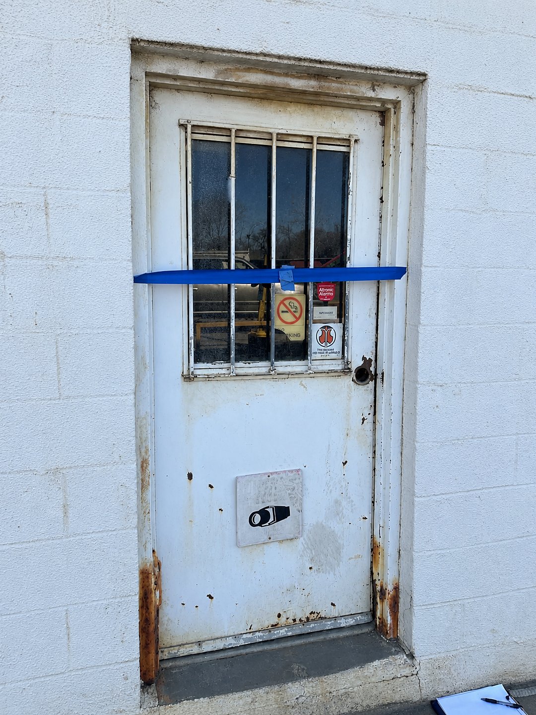 Before: a rusted white steel door with a barred window, taped shut