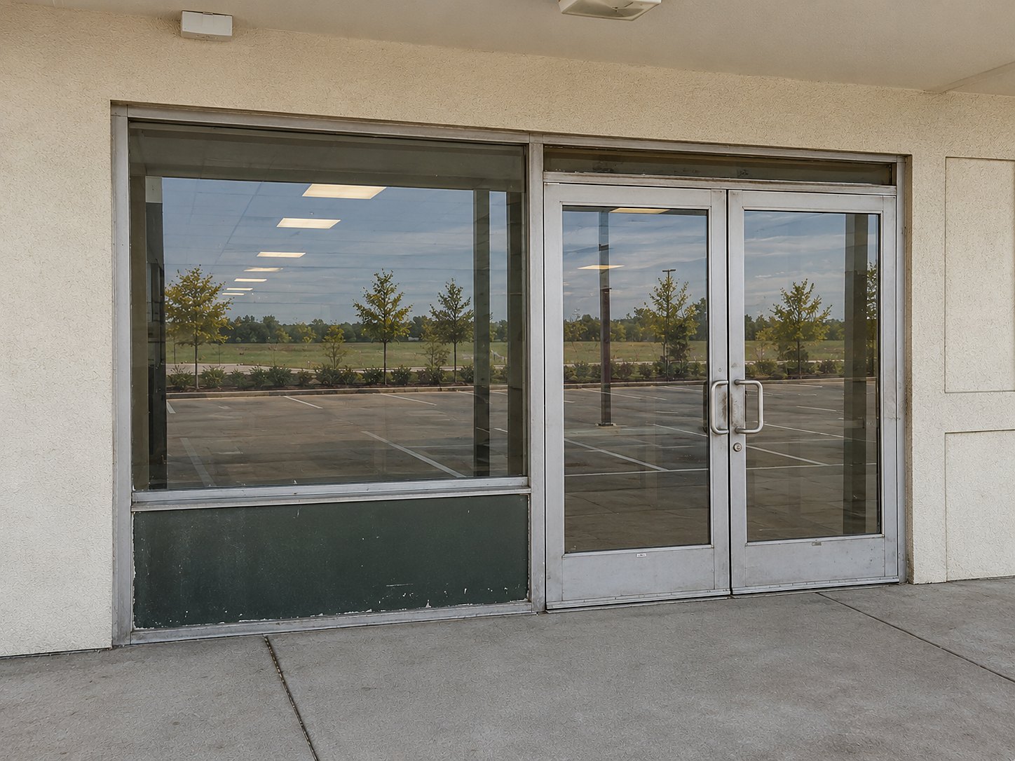 Before: the same entrance with worn, dated aluminum doors and a scuffed lower panel