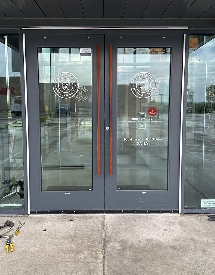 Dark bronze aluminum double storefront doors with tall wood pull handles at a restaurant
