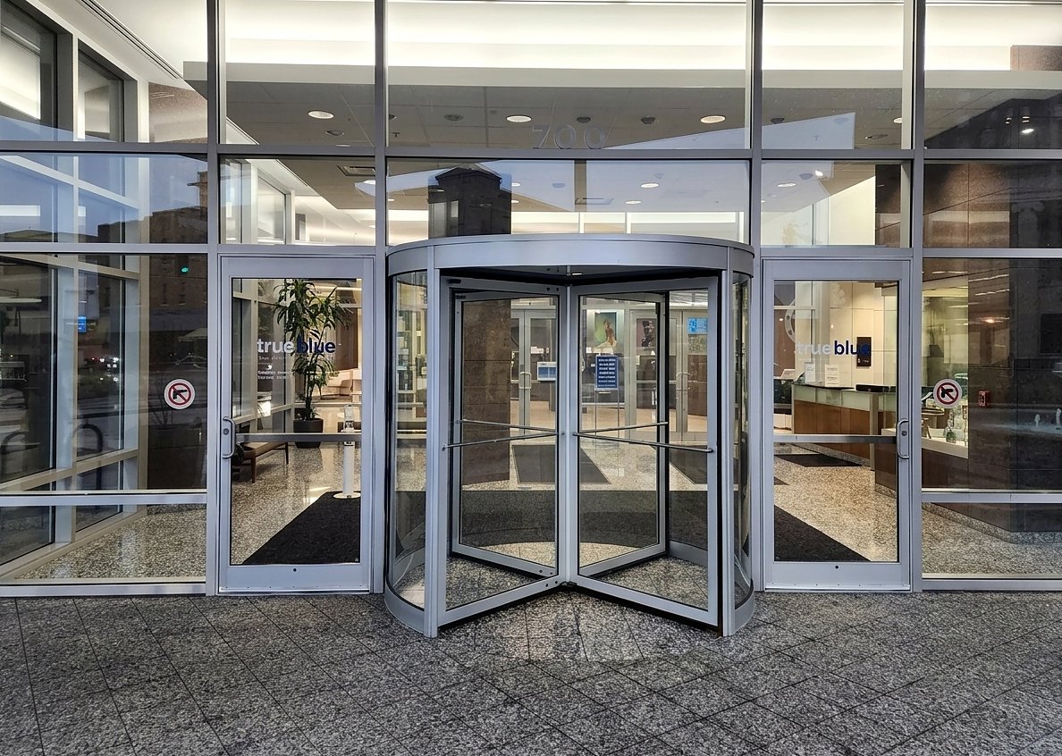 An office lobby entrance with an automatic revolving door between two glass swing doors
